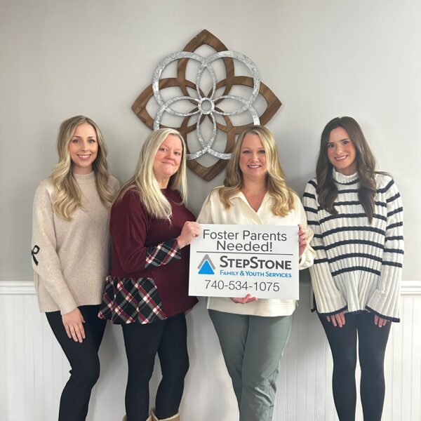 Group picture of StepStone staff holding up a "Foster Parents Needed" sign